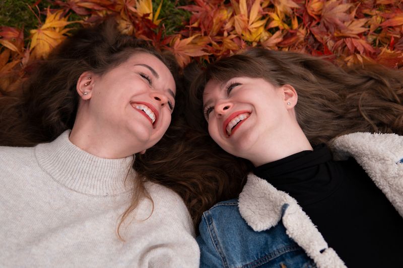 Zwei Freundinnen liegen lachend im Herbstlaub